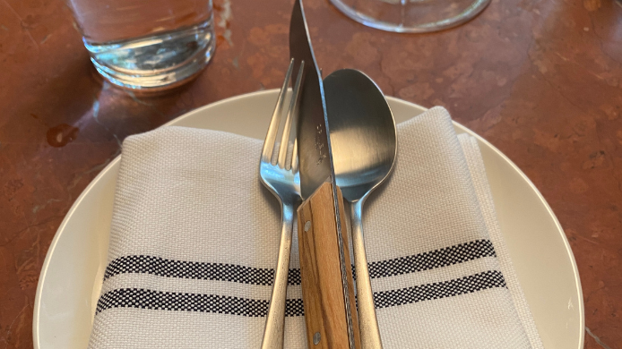 Detalle de la mesa del restaurante Piedra en Barcelona, con cubiertos sobre una servilleta de tela y vajilla preparada para el servicio.