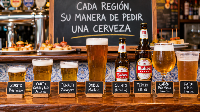 Diferentes formatos de cerveza servidos en una barra española, identificados como zurito, corto, penalti, doble, quinto, tercio, cañón y katxi.  