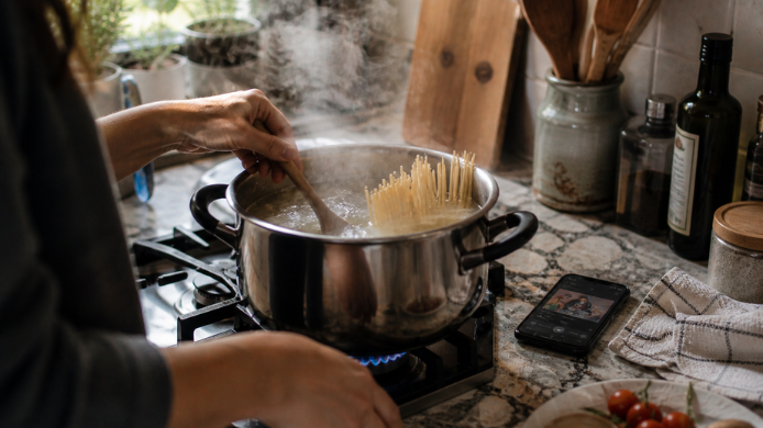 Olla con pasta hirviendo mientras se controla el tiempo de cocción con música en Soptify en la cocina