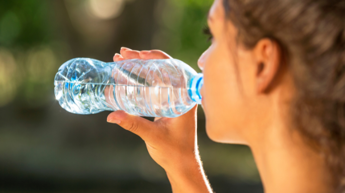 Mujer de perfil en un parque practicando el hábito saludable de beber agua de una botella.