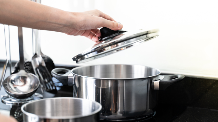 Mano levantando la tapa de una olla de acero inoxidable durante la cocción en una cocina doméstica.