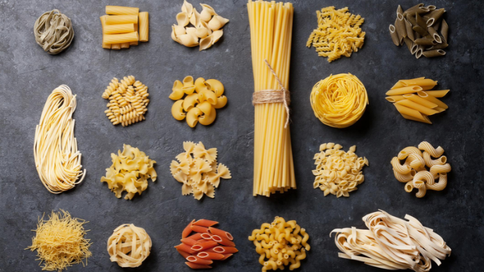 Diferentes variedades de pasta italiana, como spaghetti, penne, fusilli y tagliatelle, dispuestas sobre una mesa.