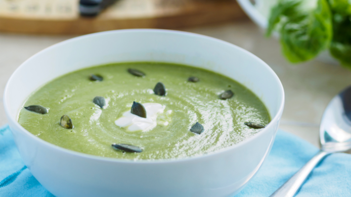 Sopa fría de aguacate servida en un cuenco blanco y decorada con semillas de calabaza y un toque de crema.