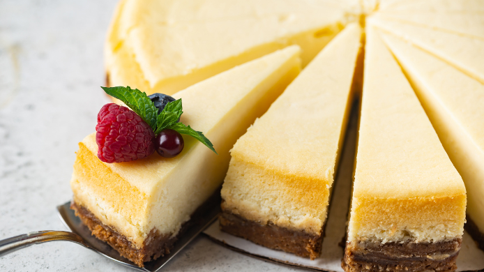 New York Cheesecake con base de galleta de jengibre y porción decorada con frambuesas y arándanos.
