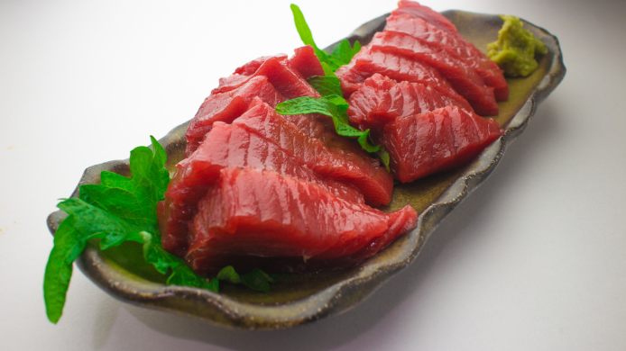 Láminas de atún rojo crudo servidas en un plato con hojas verdes y wasabi