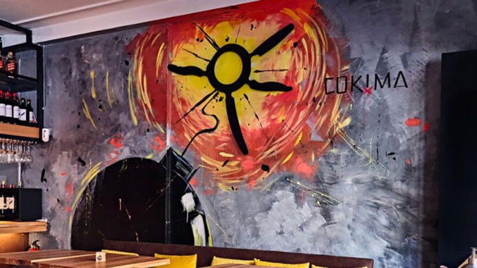 Interior del restaurante Cokima en Madrid, con un gran mural abstracto en tonos rojos, amarillos y grises junto al logotipo del local.