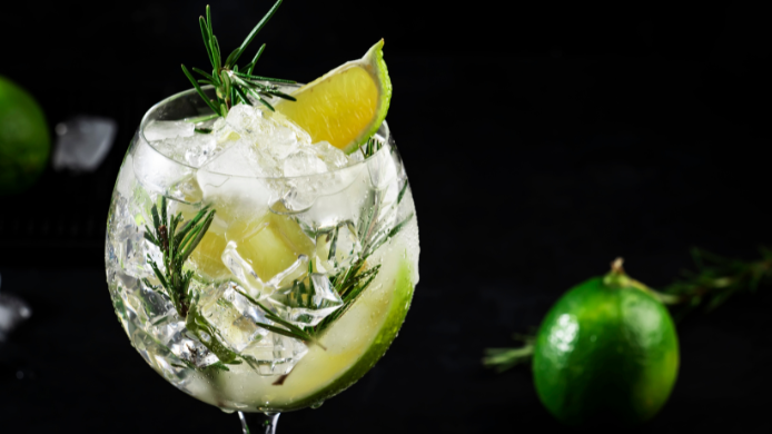 Gin tonic servido en una copa de balón, decorado con una rodaja de lima, abundantes cubitos de hielo y ramitas de romero fresco. Cócteles fáciles