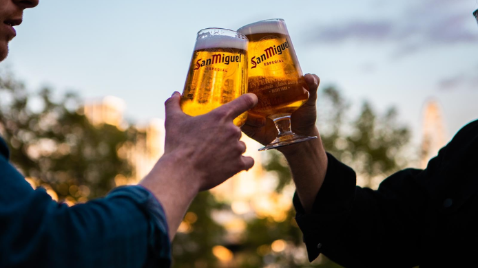 dos manos con dos copas de cerveza San Miguel brindando