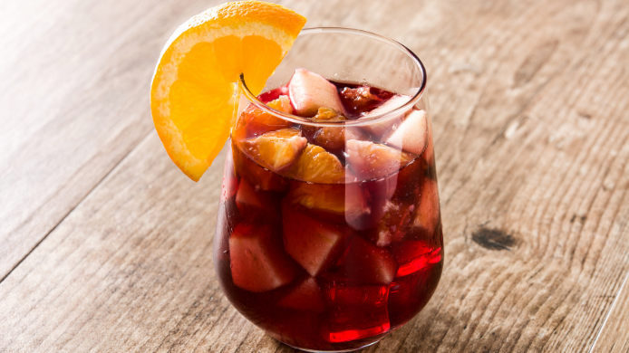 Vaso de sangría con vino tinto, frutas frescas y rodaja de naranja sobre una mesa de madera.