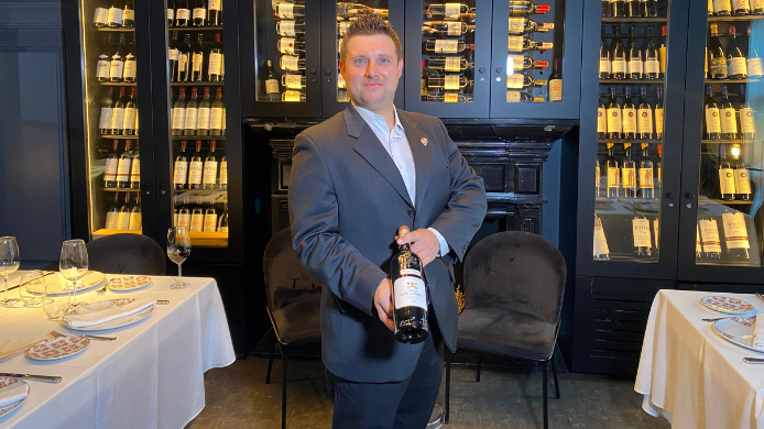Sumiller Rodrigo Sicilia sosteniendo una botella de Château Pape Clément en el restaurante Tatel con bodega de vinos al fondo
