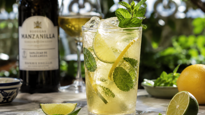 Copa de Rebujito 2.0 con hielo, lima, limón y hierbabuena junto a una botella de manzanilla