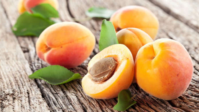 Albaricoques frescos de temporada sobre una mesa de madera rústica, uno de ellos abierto mostrando su hueso, una fruta de verano rica en betacaroteno, fibra y vitamina C.