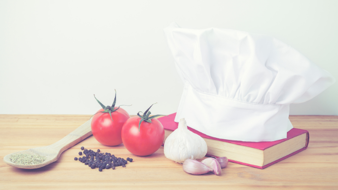 libros de gastronomía, cuchara, tomates, ajos y gorro de cocina