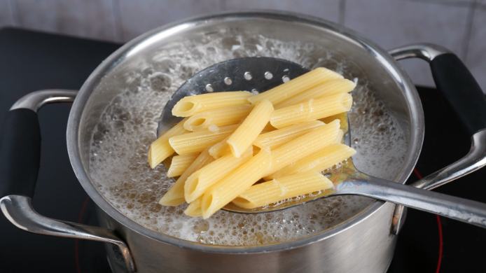 Pasta penne recién sacada del agua hirviendo para comprobar si está cocinada al dente