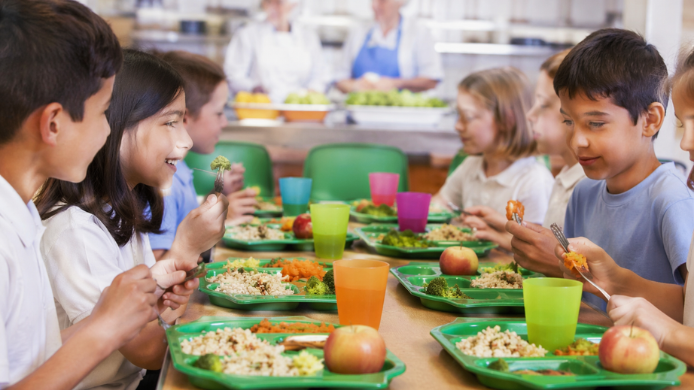 Niños comiendo en comedores escolares con menús saludables de verduras, arroz y fruta fresca