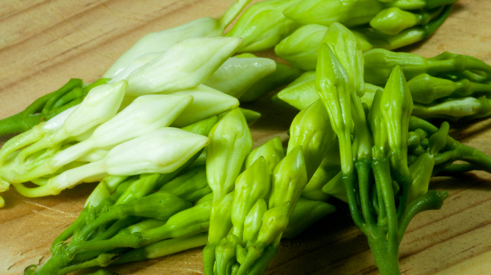 Brotes y flores frescas de loroco sobre una superficie de madera, ingrediente tradicional de la gastronomía salvadoreña.