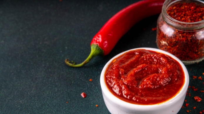 Gochujang servido en un cuenco blanco junto a chile rojo y copos de chile sobre fondo oscuro