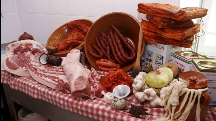 Mesa tradicional de matanza del cerdo con embutidos frescos, jamón crudo, panceta, ristras de ajos, cebollas y botes de pimentón