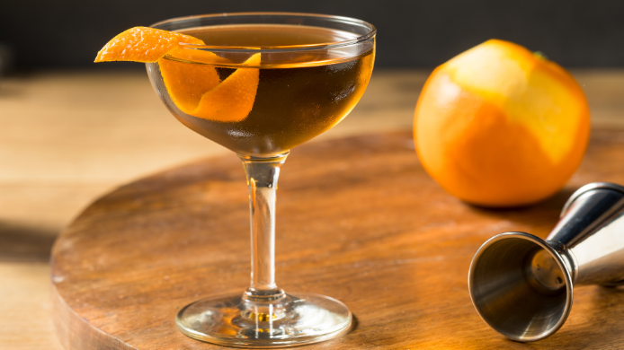 copa con cóctel Hanky Panky,, naranja y medidor sobre una mesa