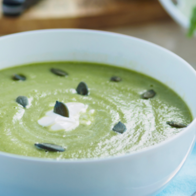Sopa fría de aguacate servida en un cuenco blanco y decorada con semillas de calabaza y un toque de crema.